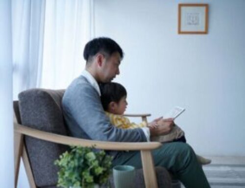 Parent reading a book with a young child while sitting together in a cozy, sunlit room.